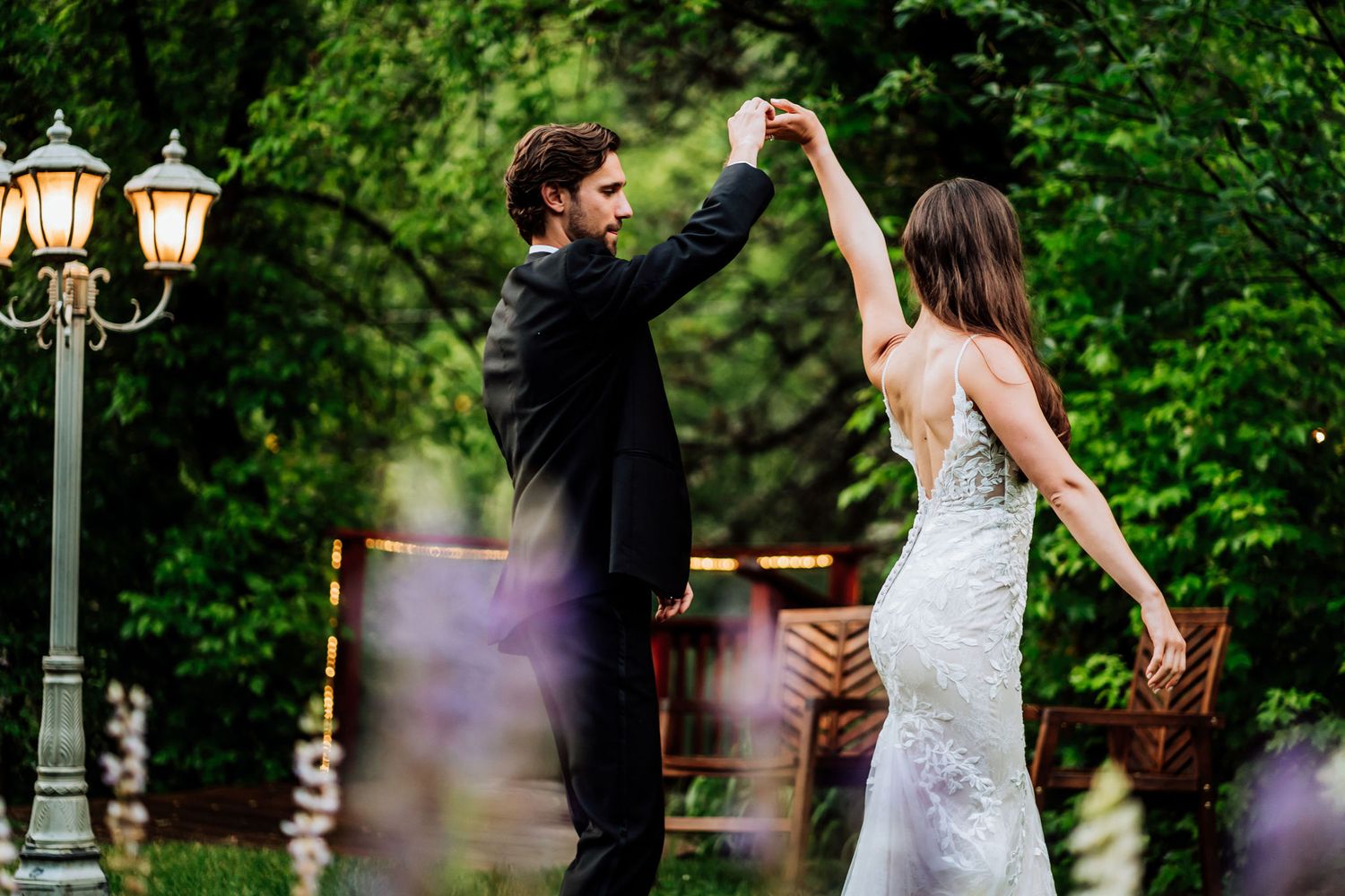 Couple dancing romantically in a garden setting with vintage lamp posts in the background.