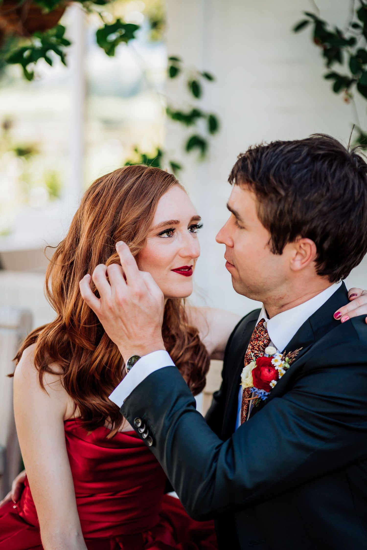 An intimate moment between a couple in formal wear, with her in a red dress and him in a dark suit.
