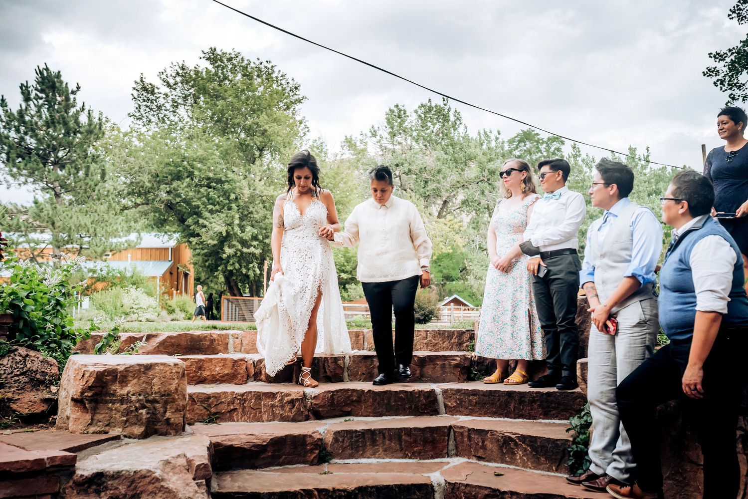 Wedding party members stand on rustic stone steps during an outdoor ceremony.