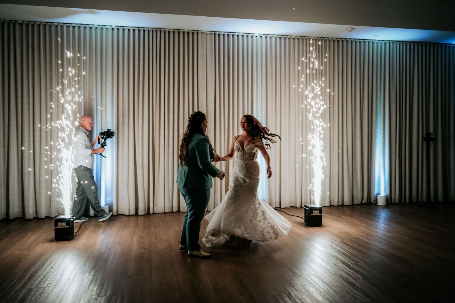 Two brides dancing joyfully with cold sparkler effects while a photographer captures the moment nearby.