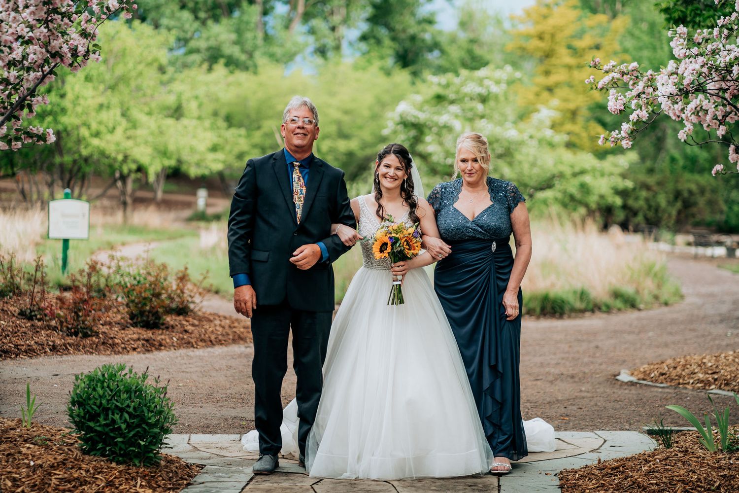 Wedding party walking together on stone path through blooming garden.