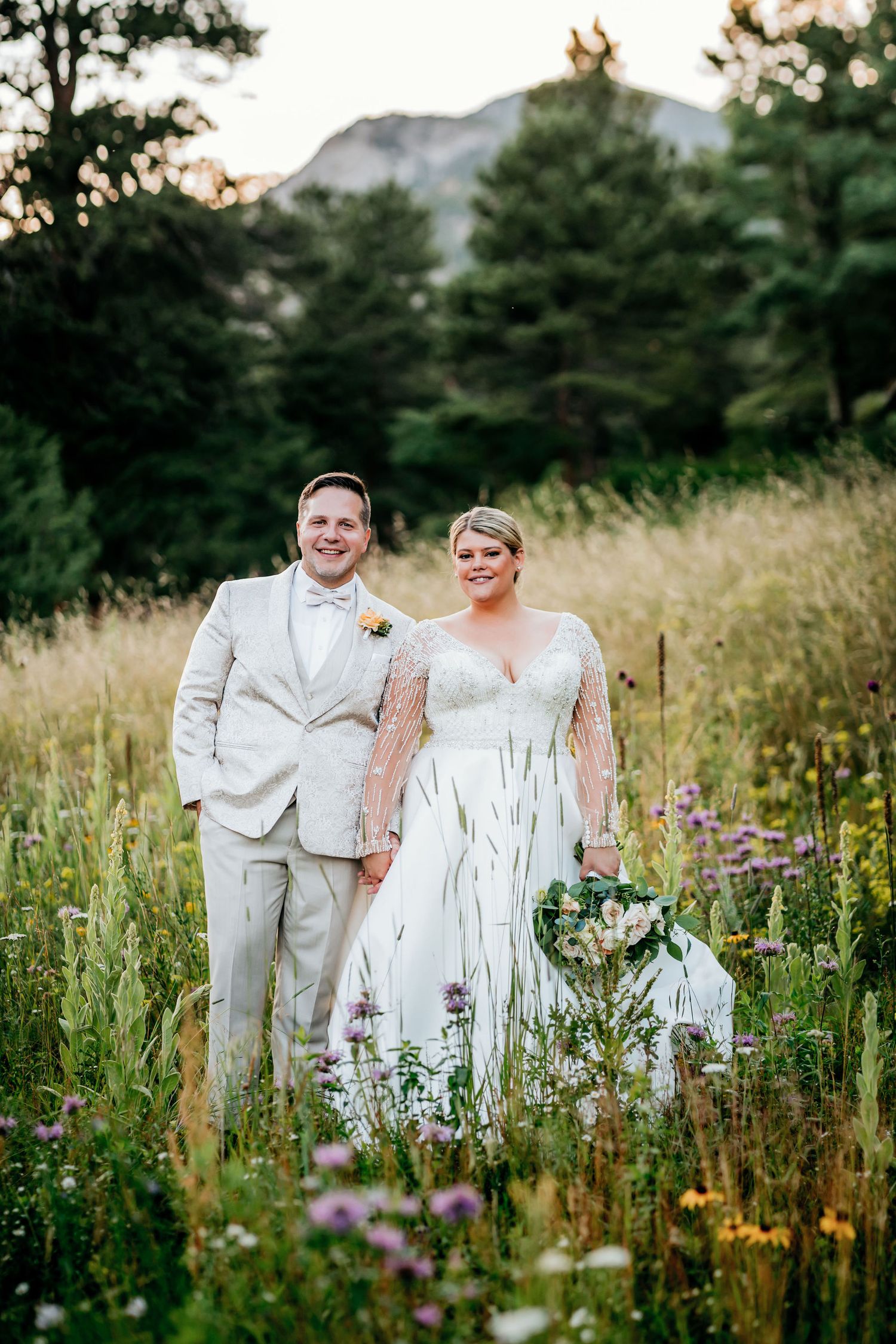 Couple poses in mountain meadow with wildflowers during golden hour.