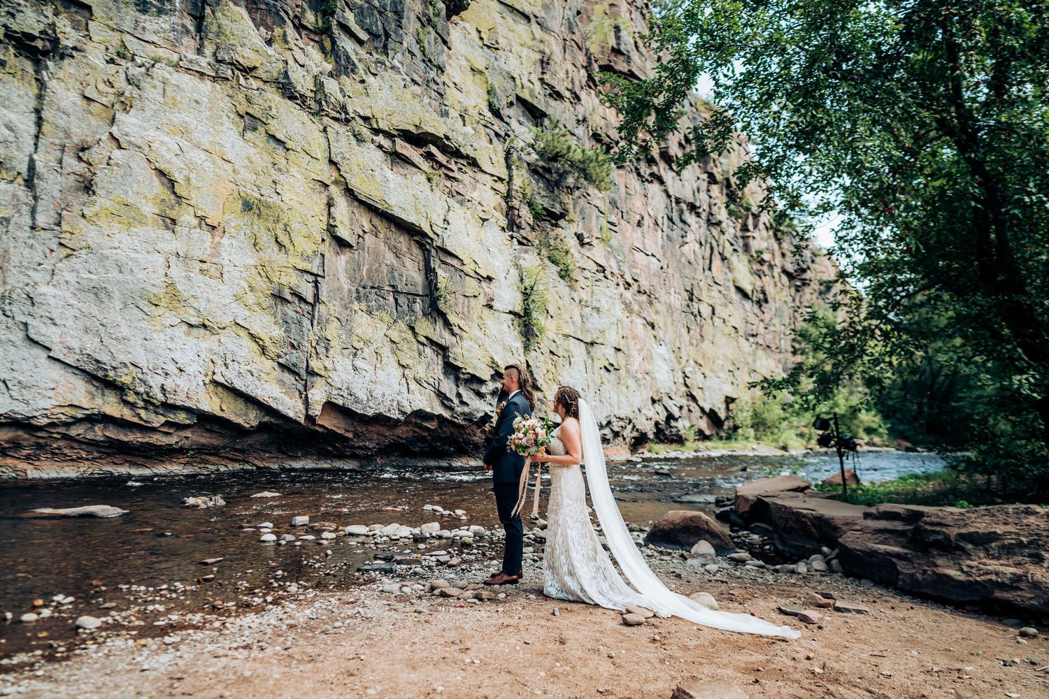 Scenic wedding portrait against towering limestone cliffs and flowing river.