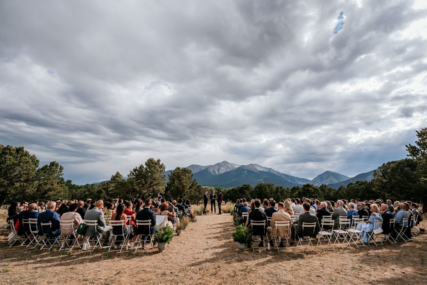 A wedding ceremony setup with rows of chairs outdoors facing mountain views under dramatic clouds.