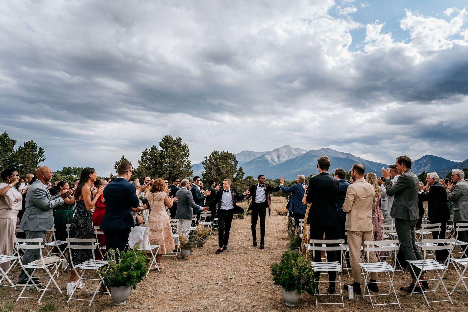 Wedding ceremony setup with white chairs and mountain vista backdrop under dramatic cloudy skies.