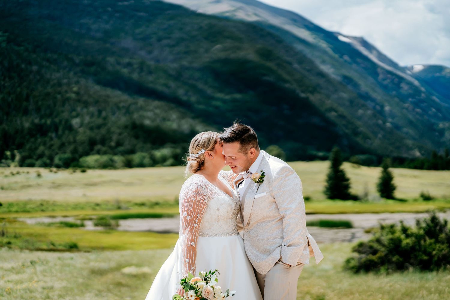 A couple embraces against a backdrop of mountain valleys and rolling hills.