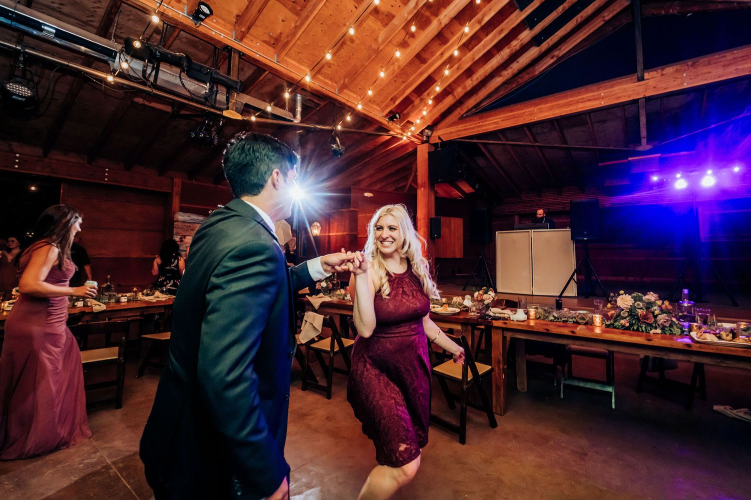 Couples dance together at a reception venue decorated with warm lighting and wooden beams.