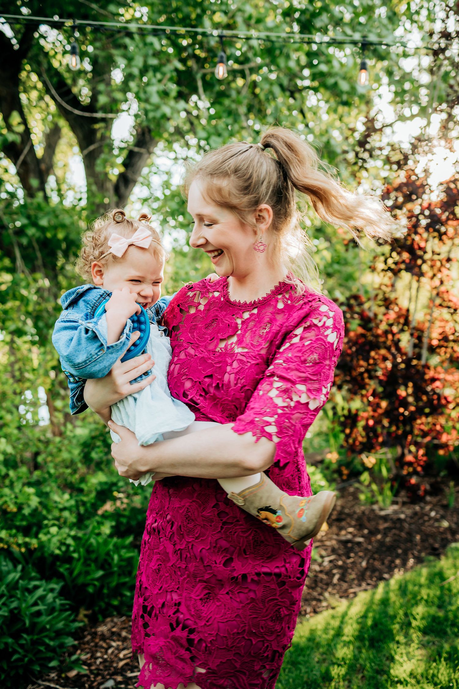A sweet moment captured outdoors with a pink lace dress against lush green foliage.