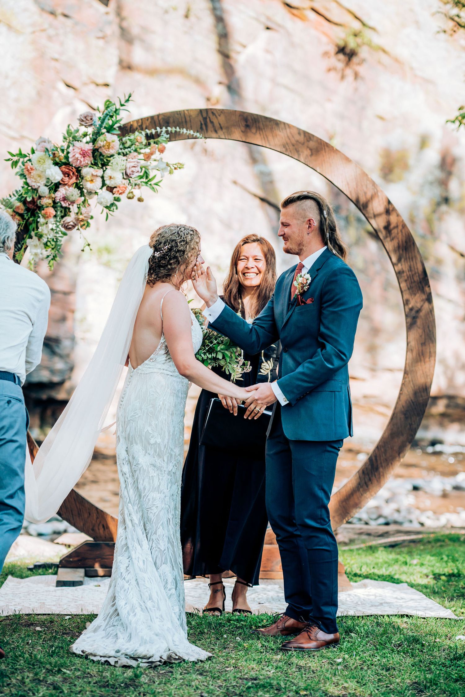 Outdoor wedding ceremony under decorated circular arch with floral arrangements.