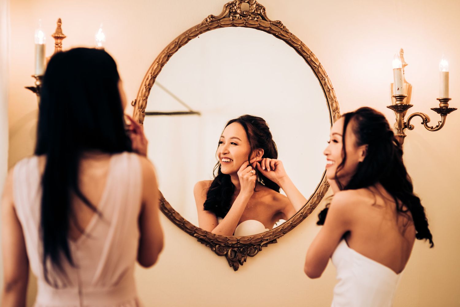 A reflection in an ornate gold mirror shows a joyful moment during wedding preparation.