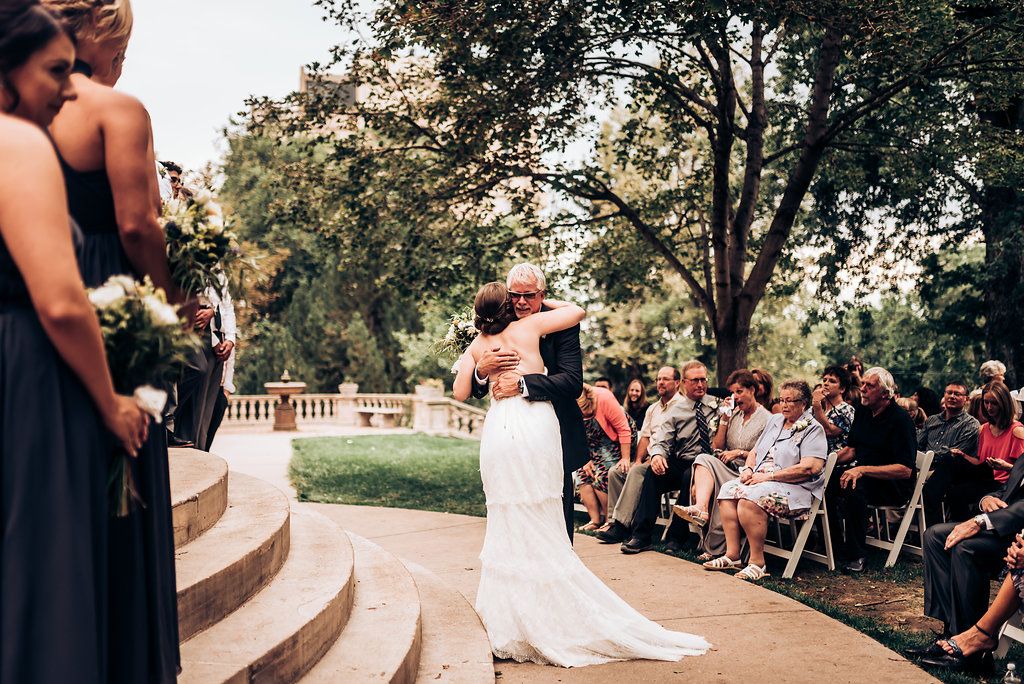 An outdoor wedding ceremony unfolds on curved stone steps with guests seated on the lawn.