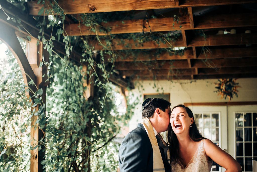 A joyful couple shares a candid laughing moment under a vine-covered pergola.