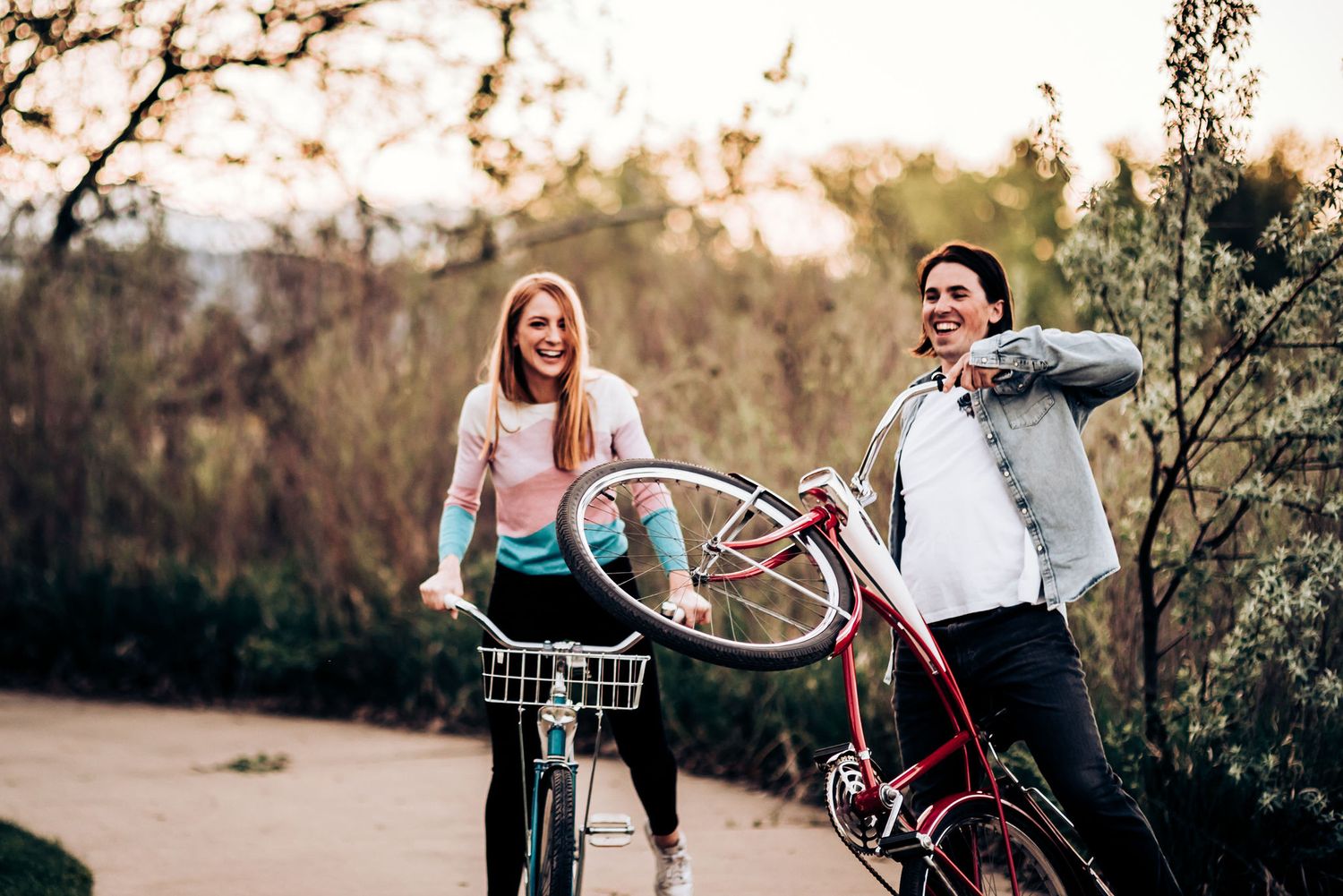 Two people laugh while biking together during golden hour on a trail.
