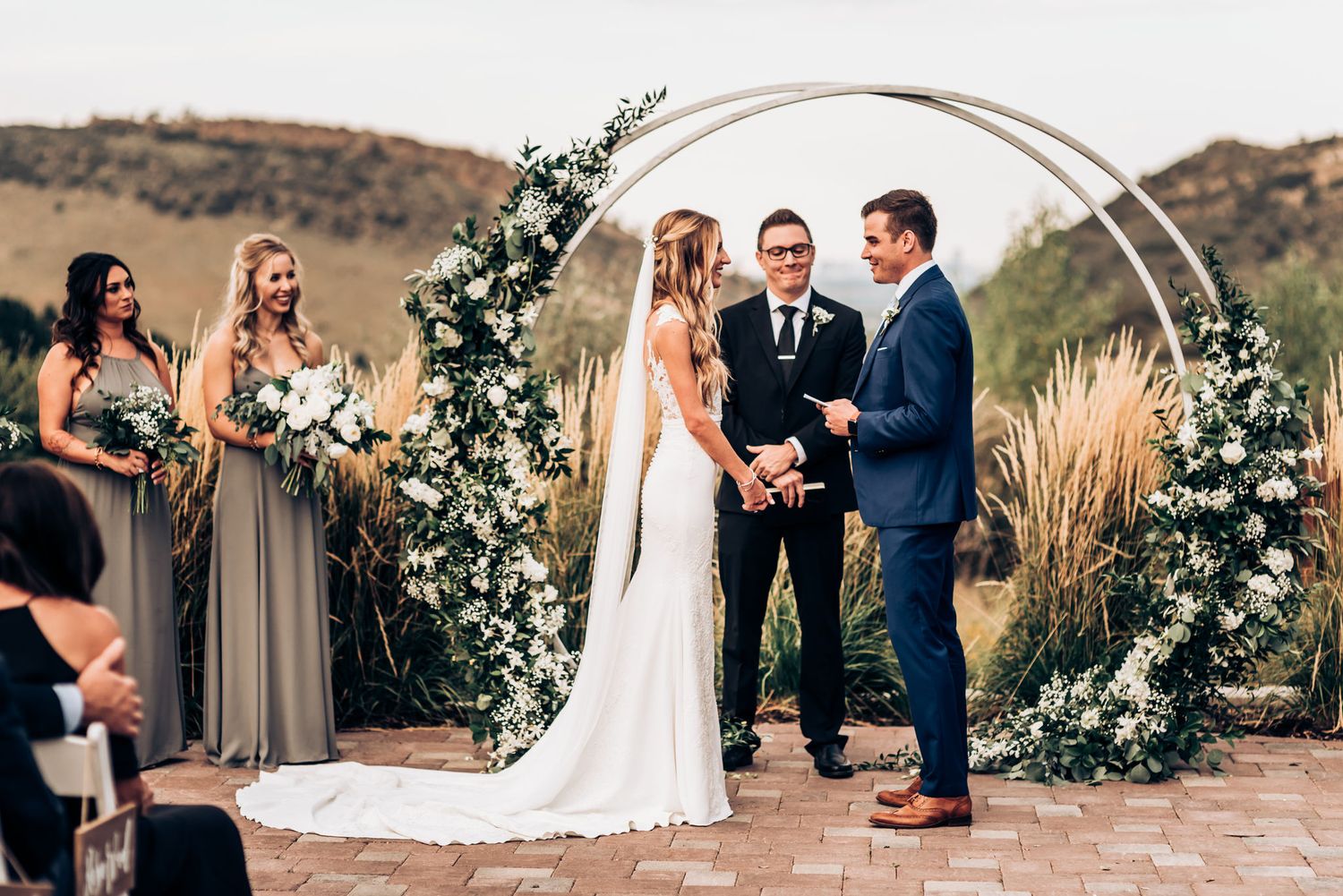 Intimate wedding ceremony moment under decorated circular arch with bridesmaids in taupe dresses.