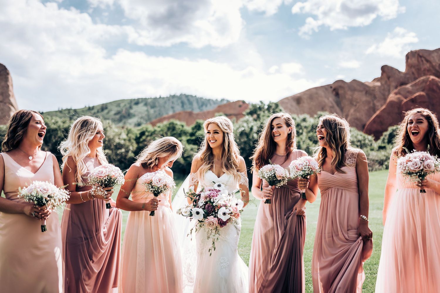 Bridal party poses against scenic red rock formations wearing blush and pink gowns.
