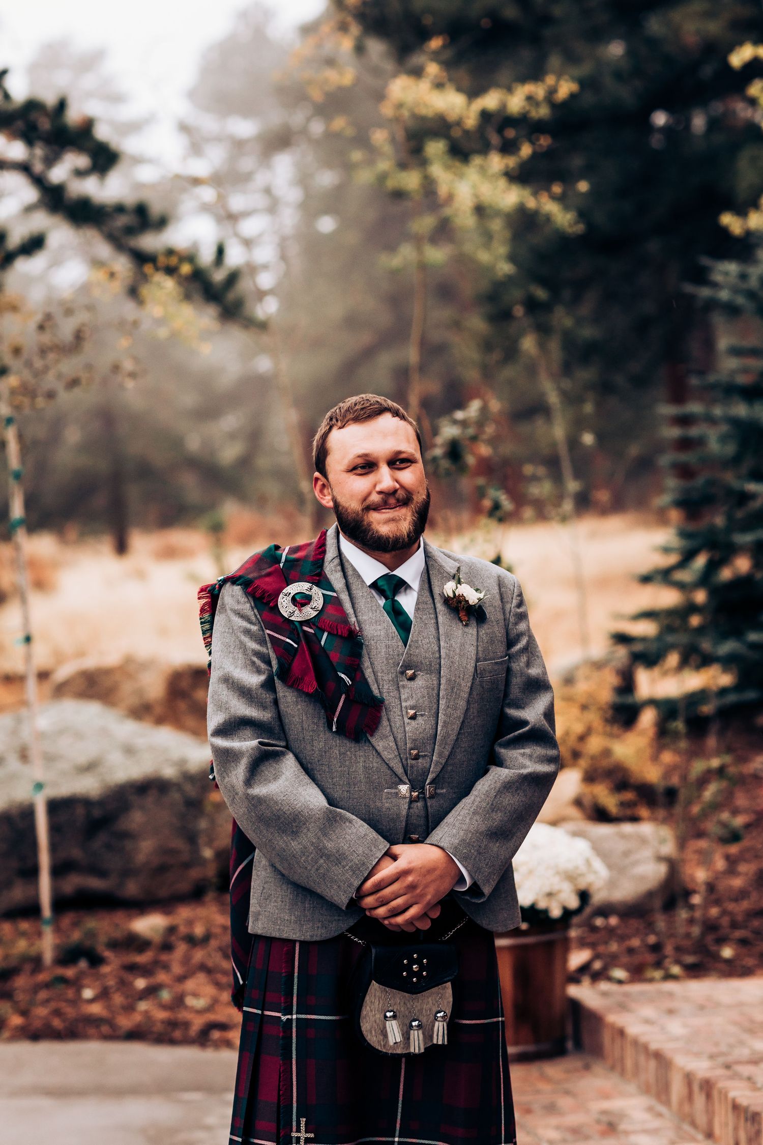 Groom in traditional Scottish attire smiles warmly during an autumn outdoor wedding.