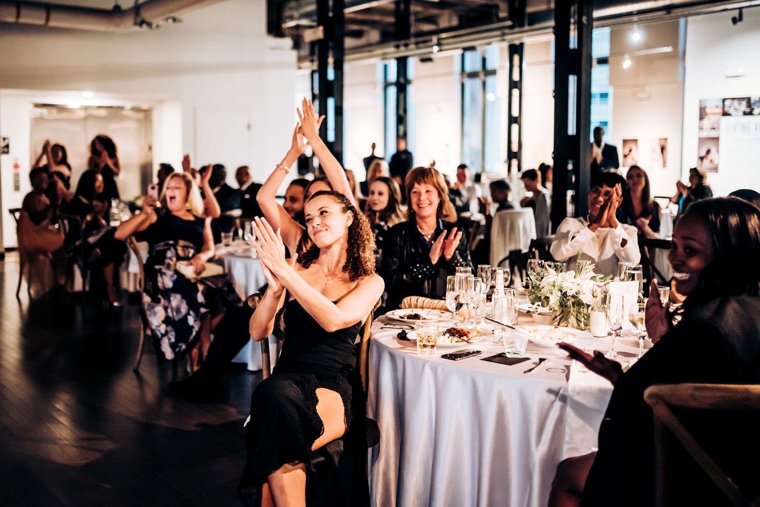 Wedding reception guests stand and cheer during celebratory moment in modern venue.