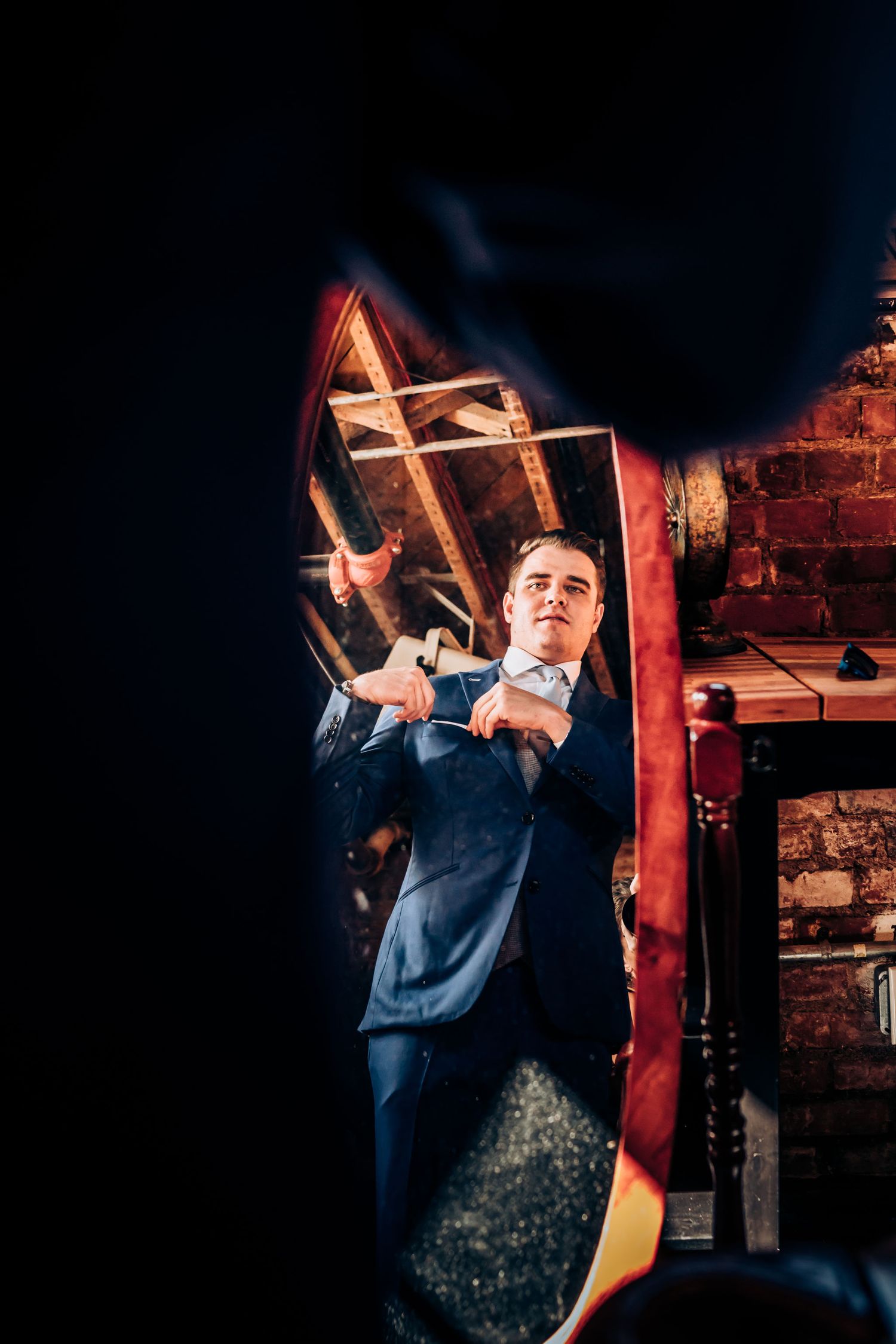 Person in navy suit making dramatic gesture in dimly lit venue with brick wall.