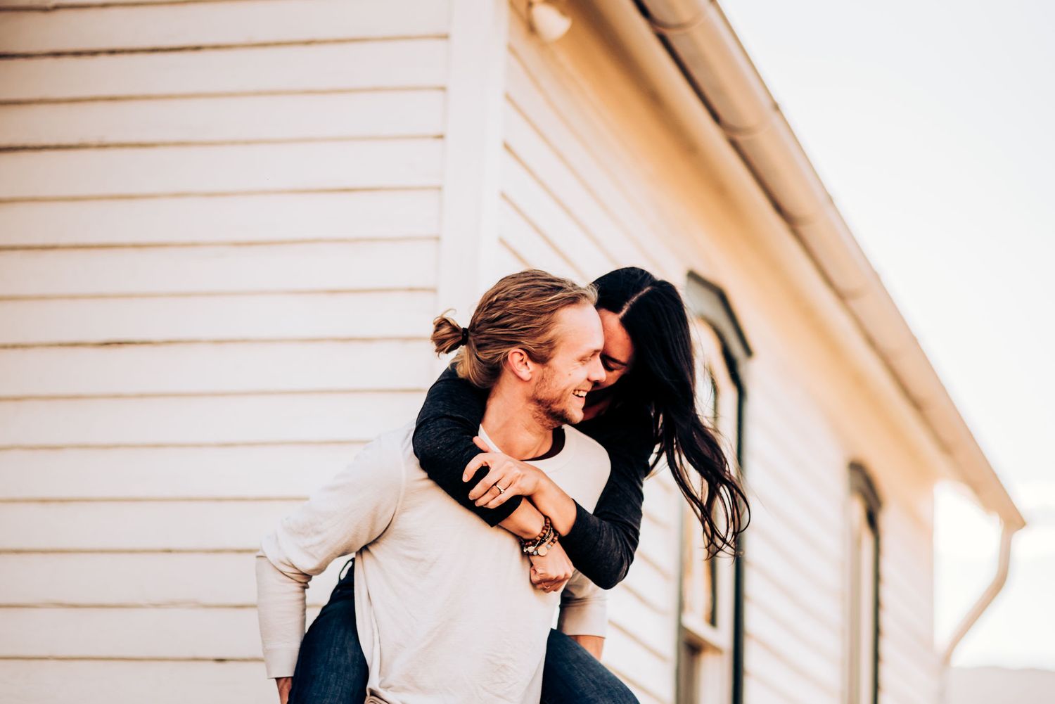 A couple shares a tender embrace against a white house exterior.