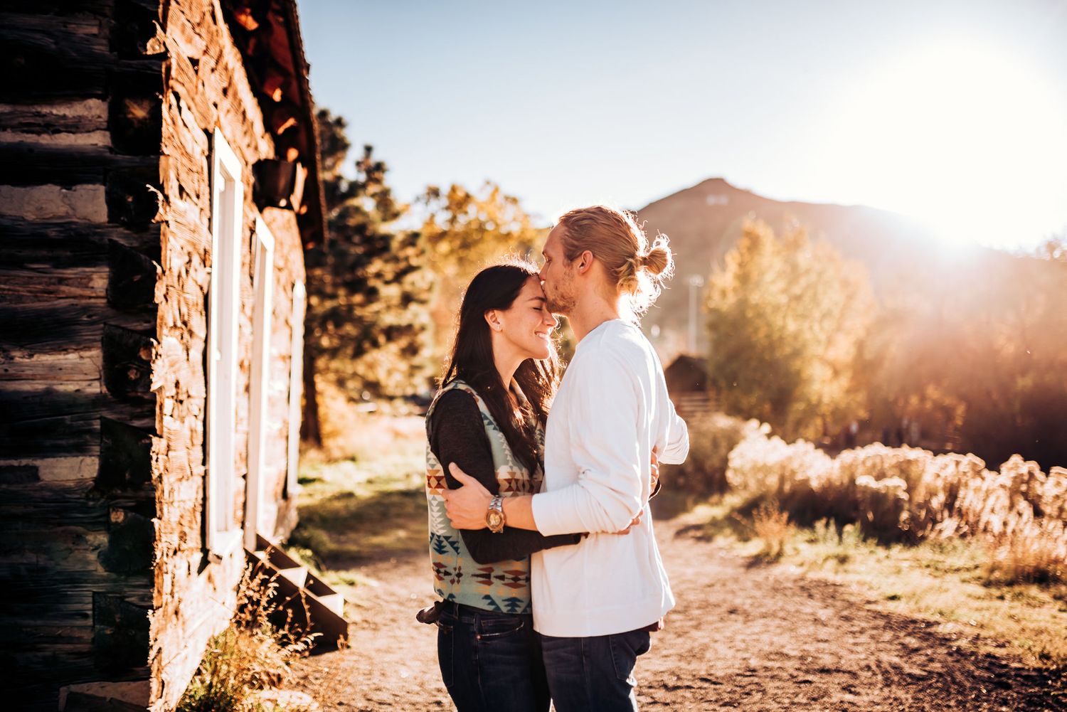 Couple sharing intimate moment outside rustic cabin with mountains in background.