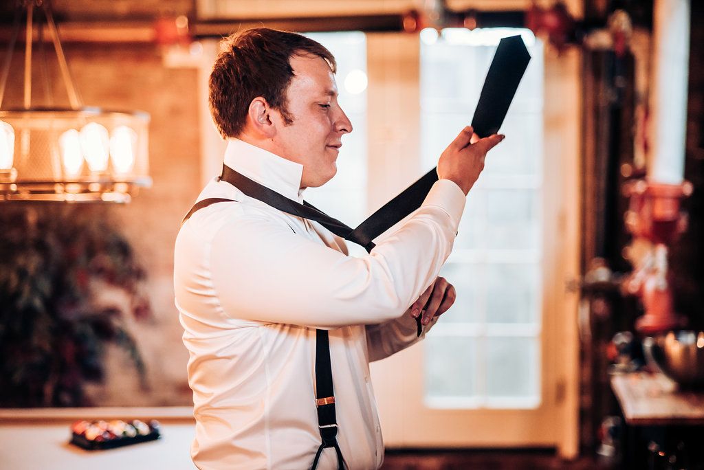 A person adjusting their tie while getting dressed in formal attire in a warm-lit room.