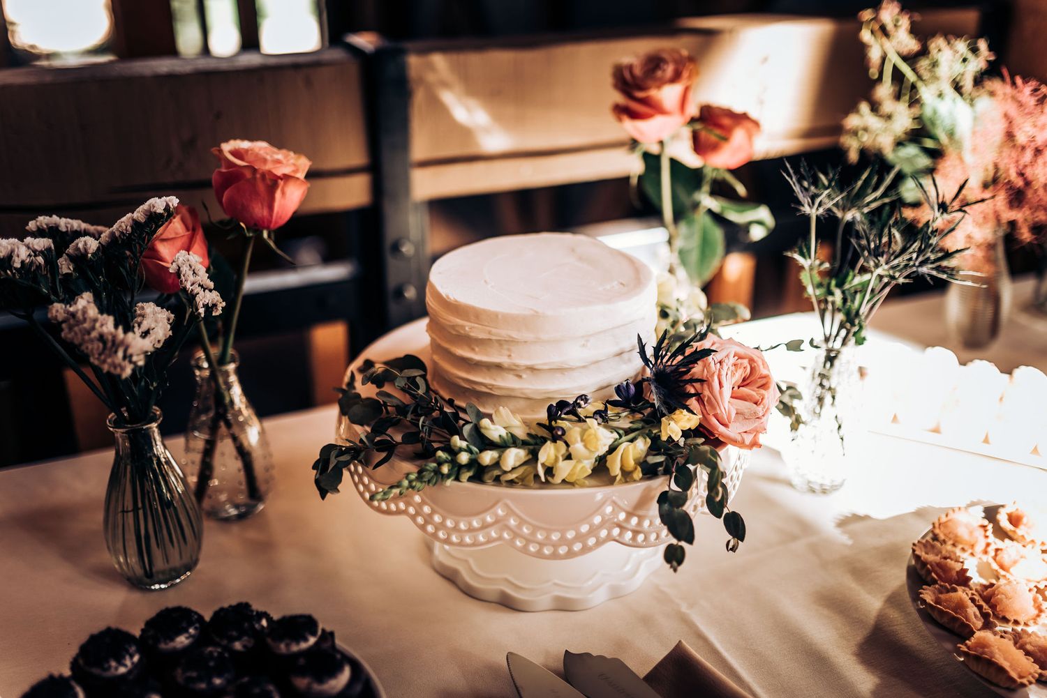 White tiered cake decorated with roses and pearls on elegant table setting.