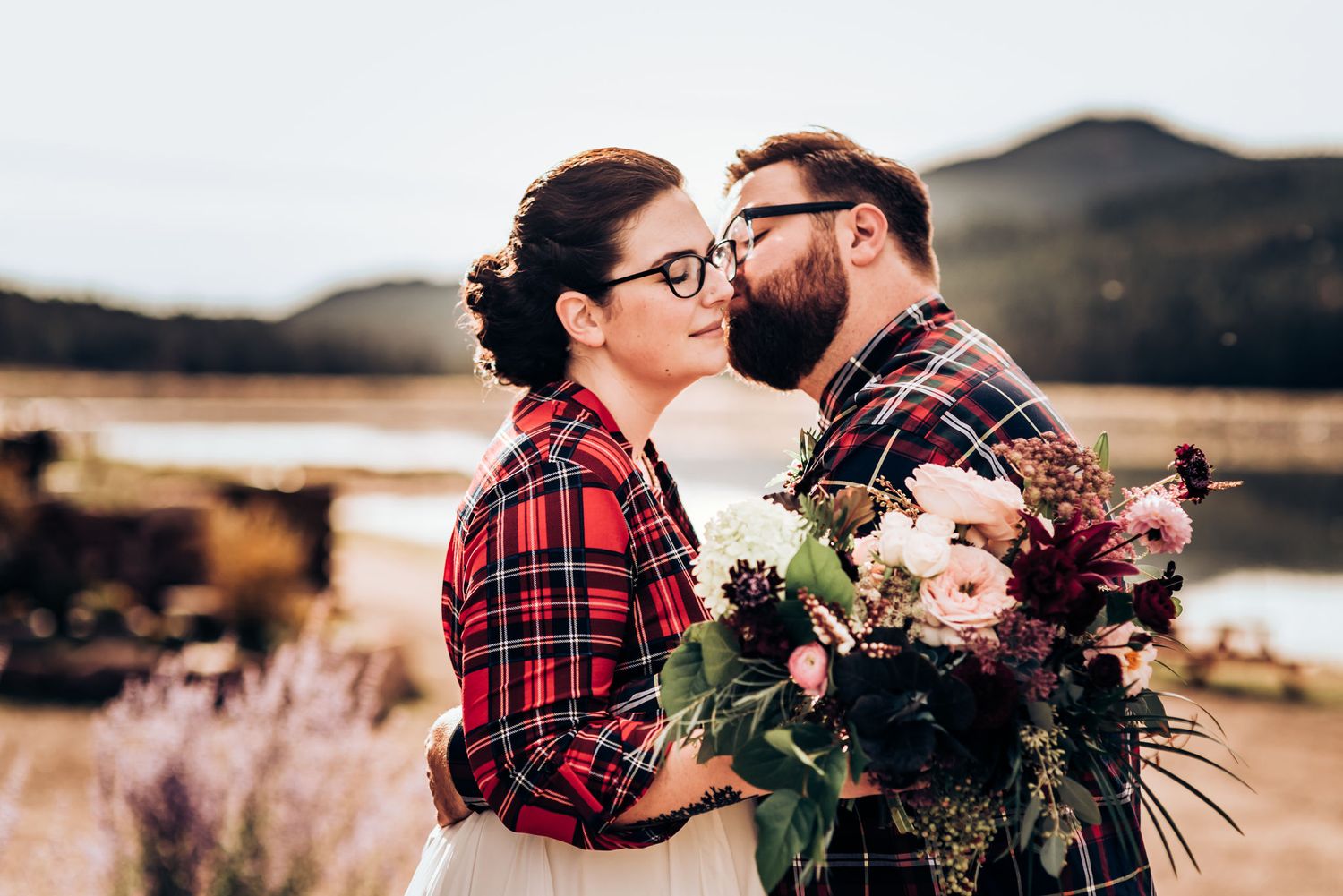 A couple shares an intimate moment with a beautiful bouquet of flowers against a mountain backdrop.