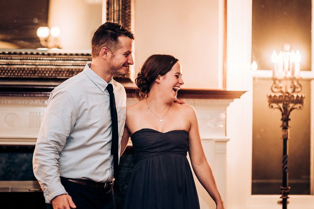 Joyful couple sharing a candid moment of laughter in an elegant venue with a chandelier and fireplace.