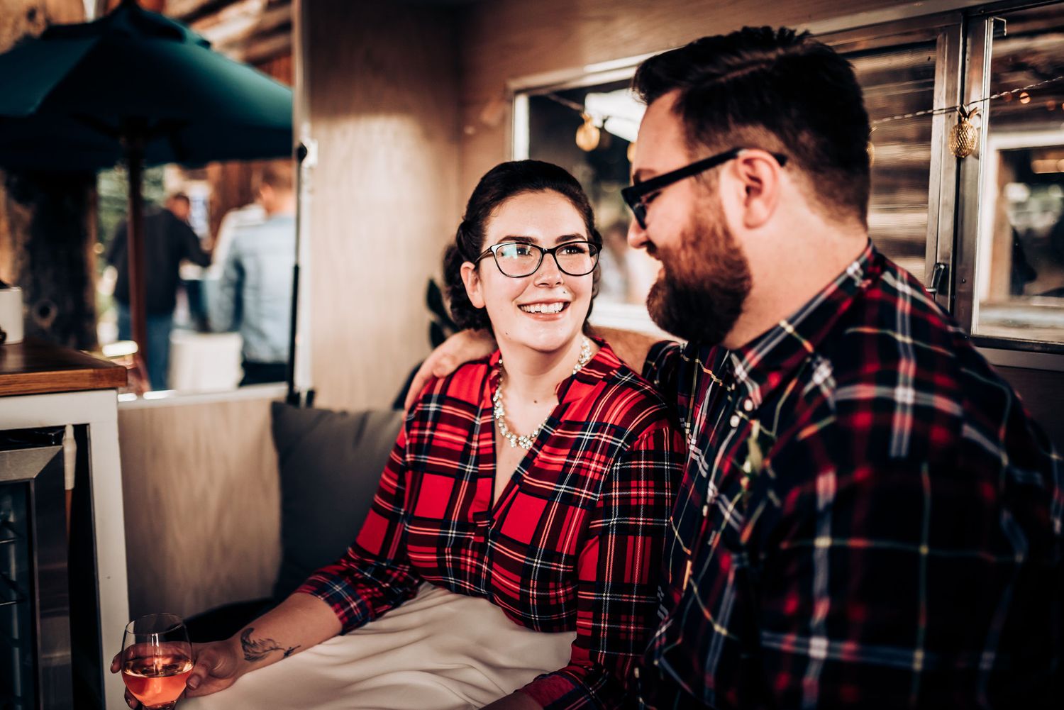 Two people in plaid shirts share a laugh while sitting together in a rustic setting.
