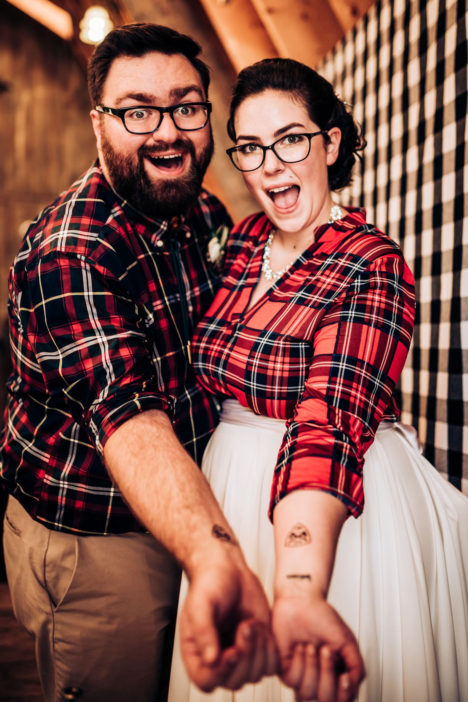 A couple wearing matching plaid shirts show off their forearm tattoos.