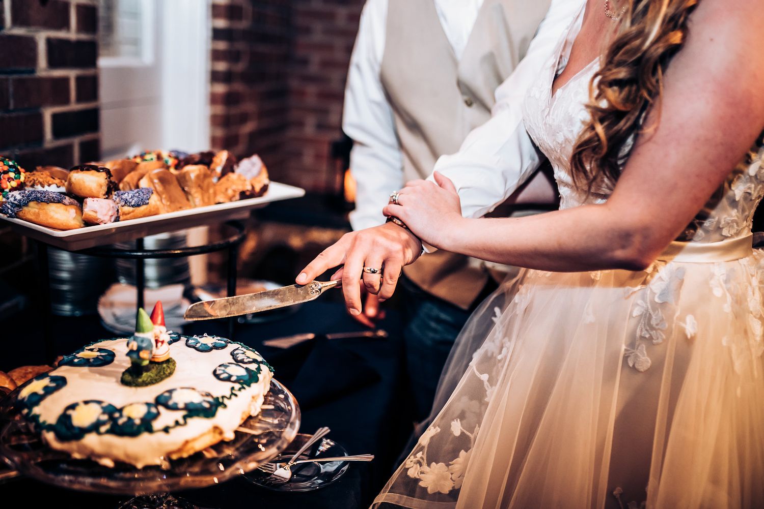 Wedding cake cutting moment with elegant desserts displayed on rustic wooden stands.