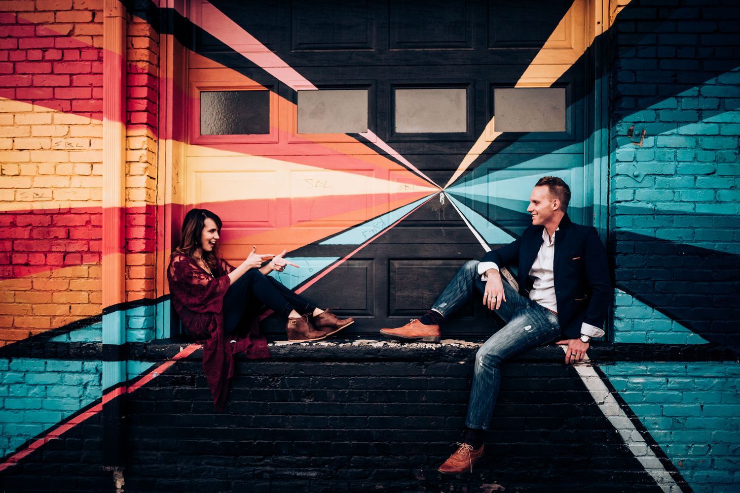 Two people sit apart on steps in a colorful hallway with geometric patterns.