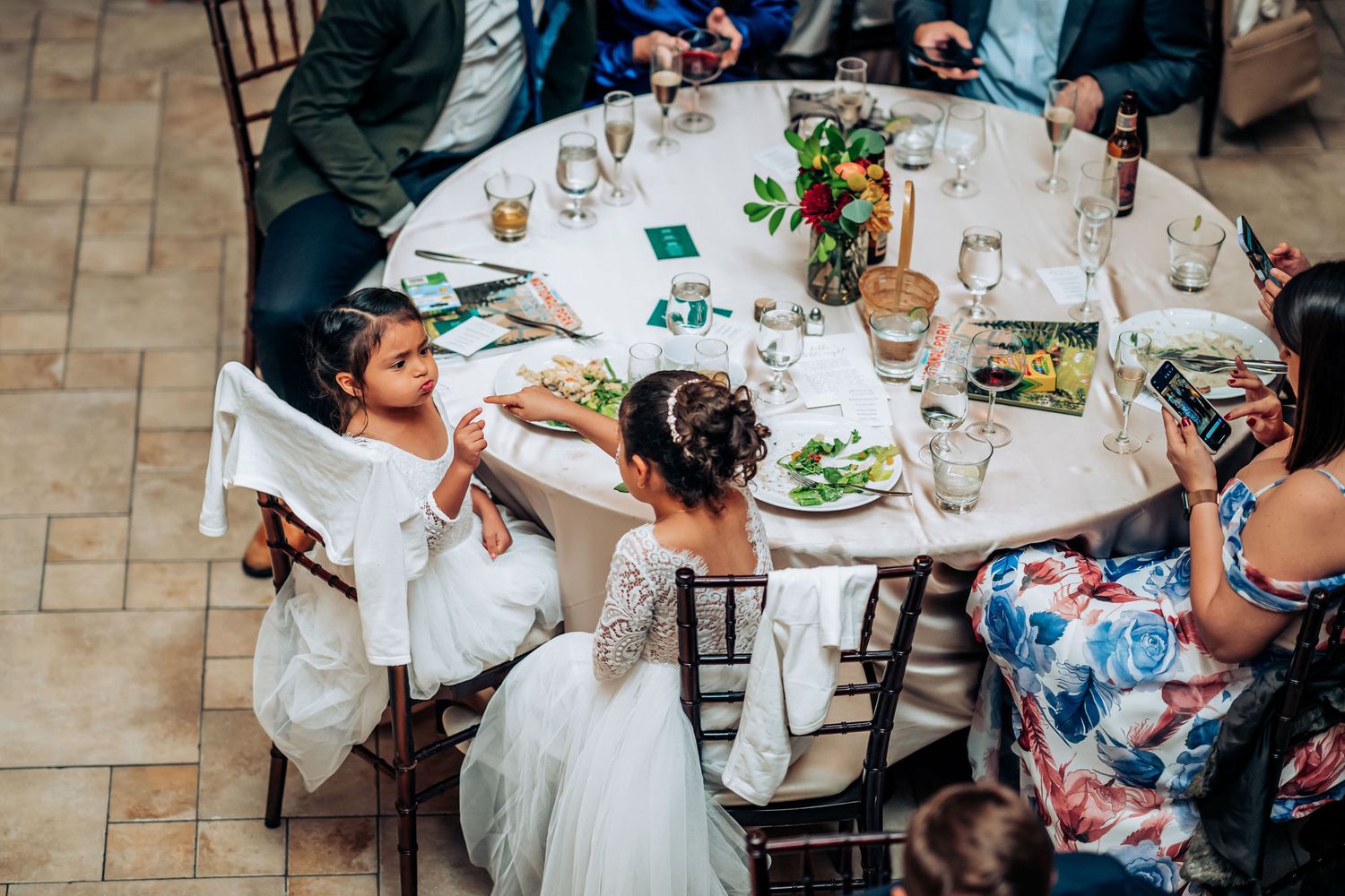 Wedding guests gather around a decorated circular table during a reception celebration.