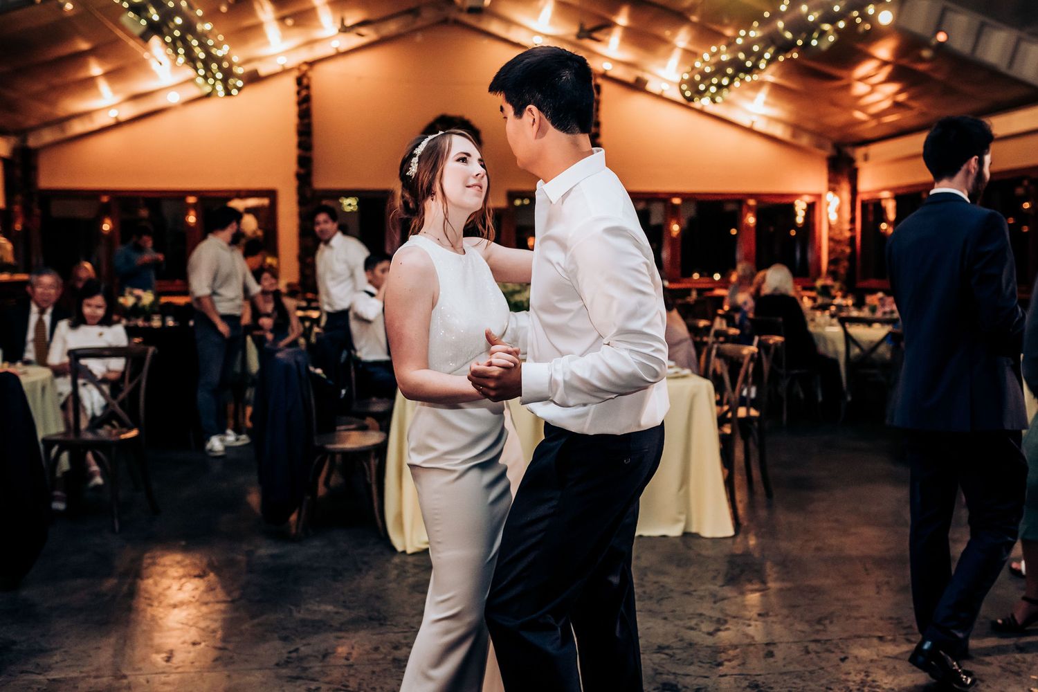 Couple shares an intimate slow dance in a warmly lit reception hall.