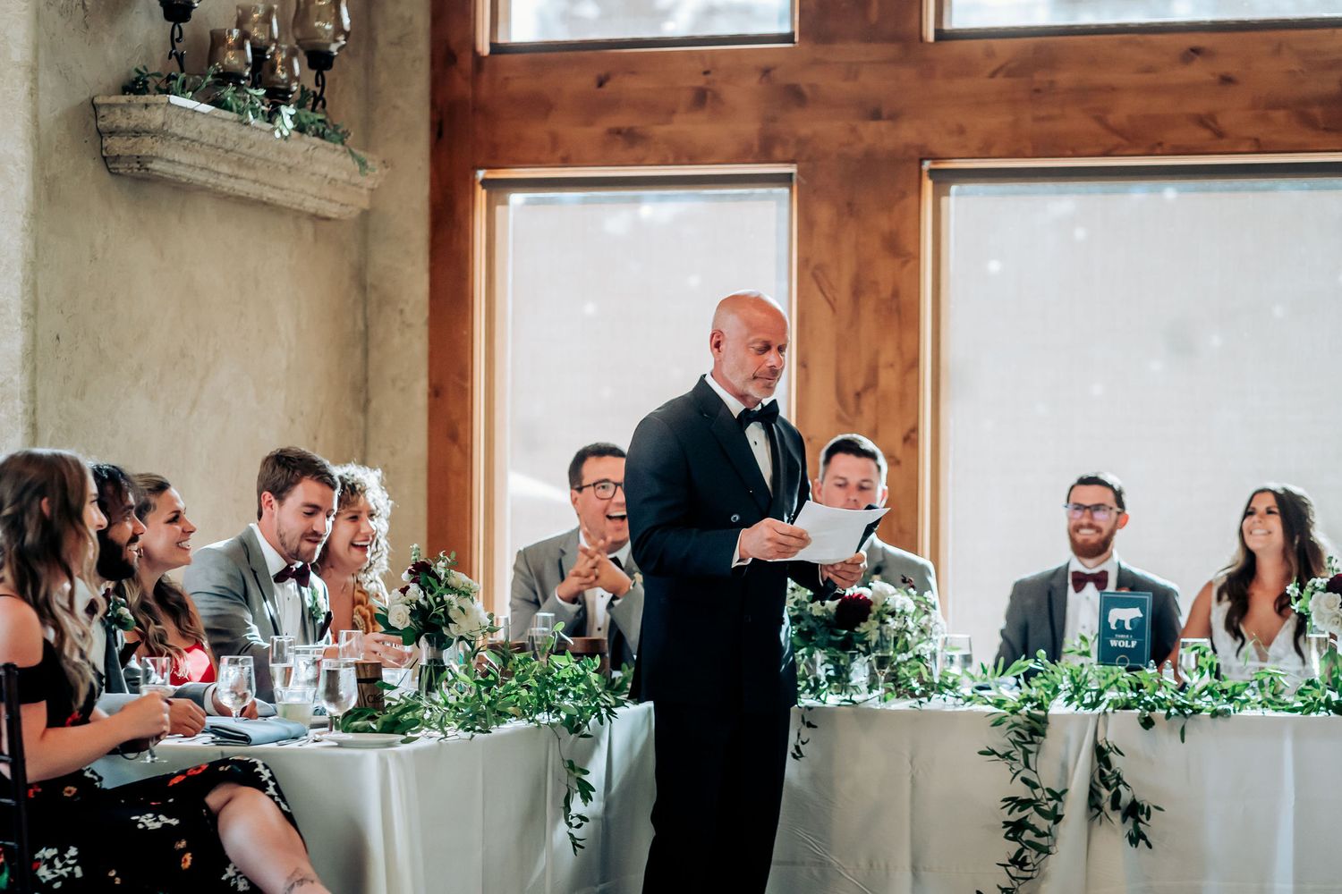 A speaker delivers a heartfelt speech at a wedding reception with guests seated at decorated tables.