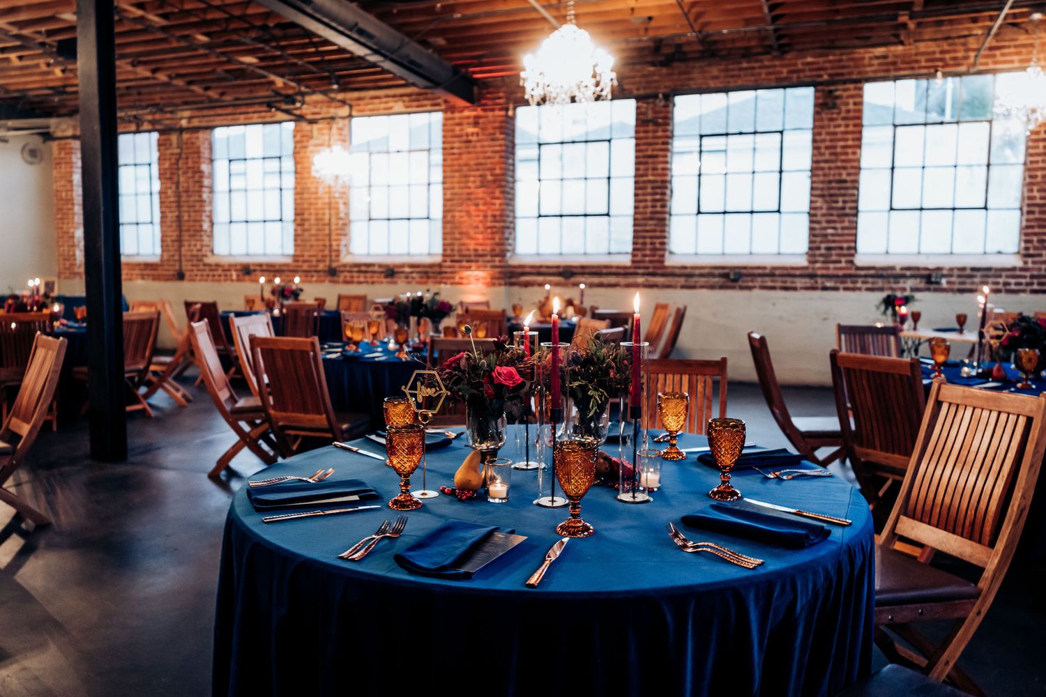 Reception hall with wooden chairs and navy blue tablecloths set for wedding celebration.