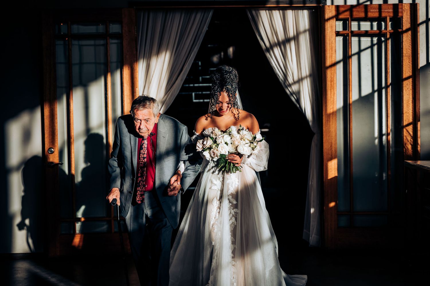 Wedding processional scene with dramatic lighting and shadows in an indoor venue.