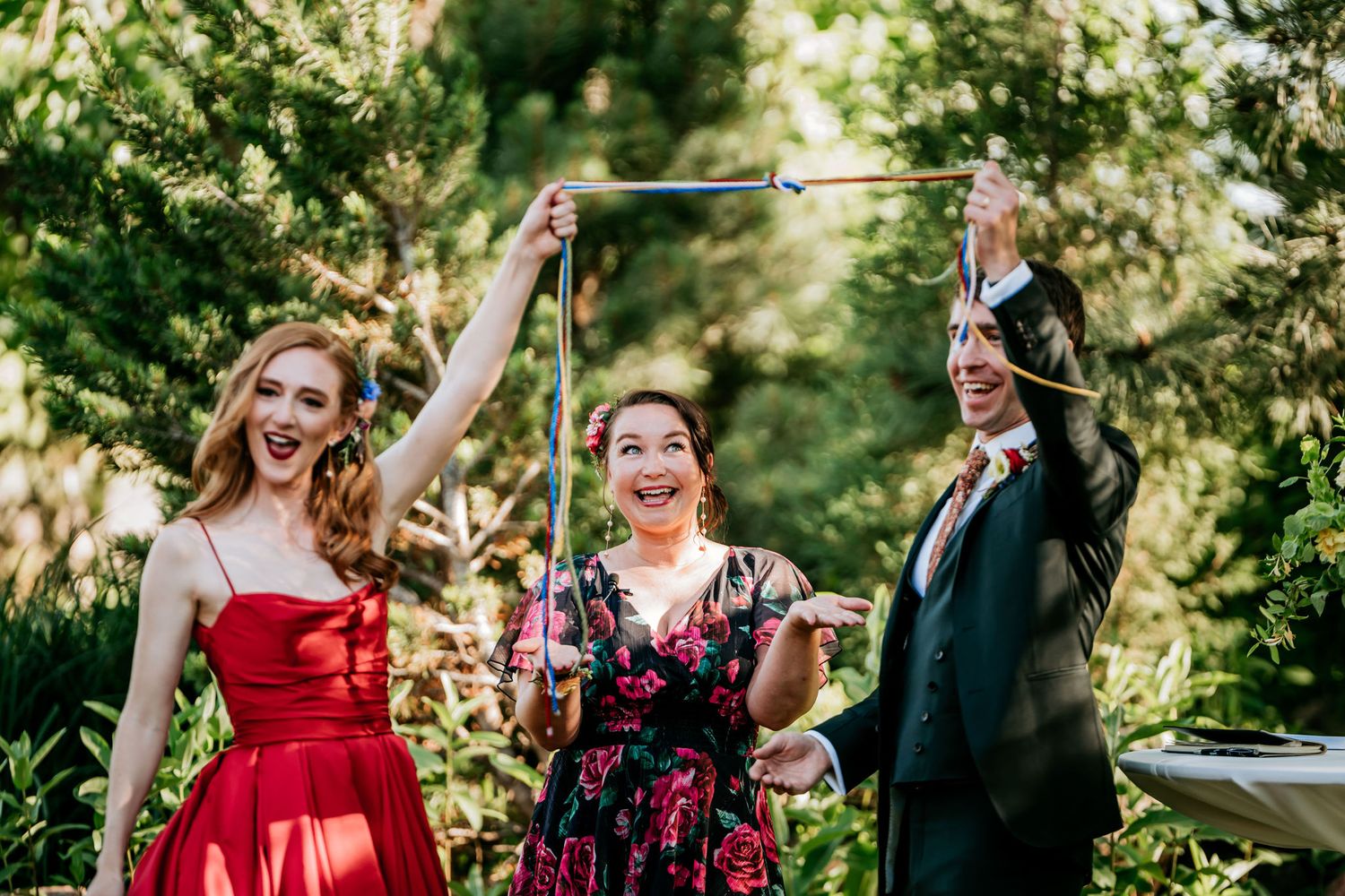 Three people celebrate joyfully with raised arms against a sunlit outdoor backdrop.