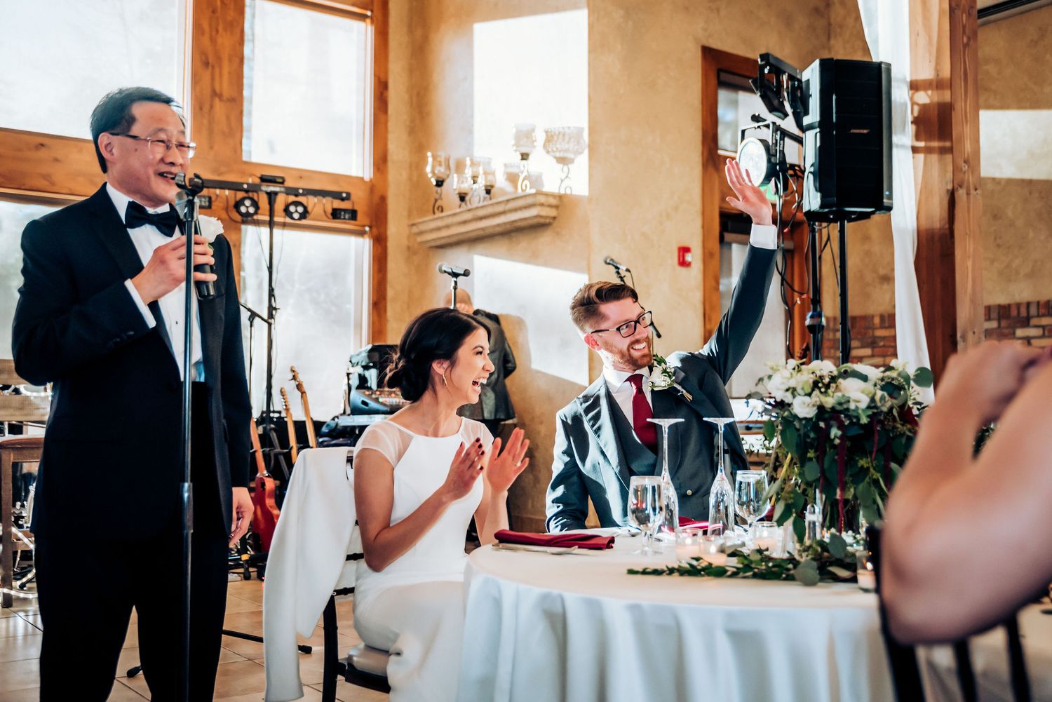 Wedding reception speech being given in rustic wooden venue with decorative lighting.
