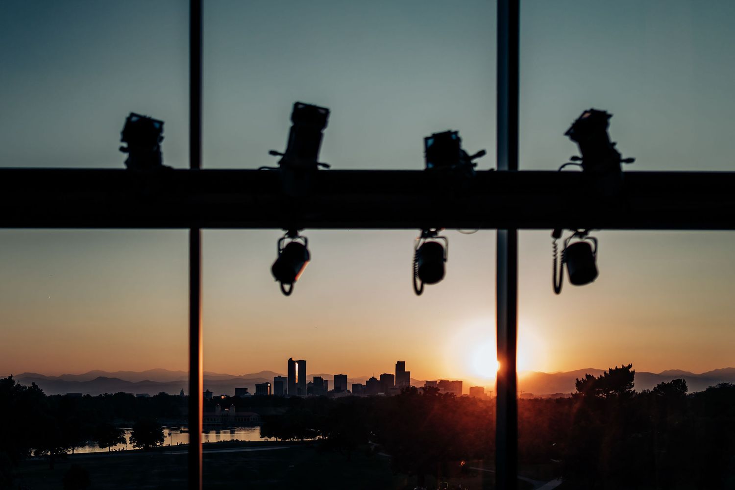 Event lighting equipment silhouetted against sunset skyline through window panes.