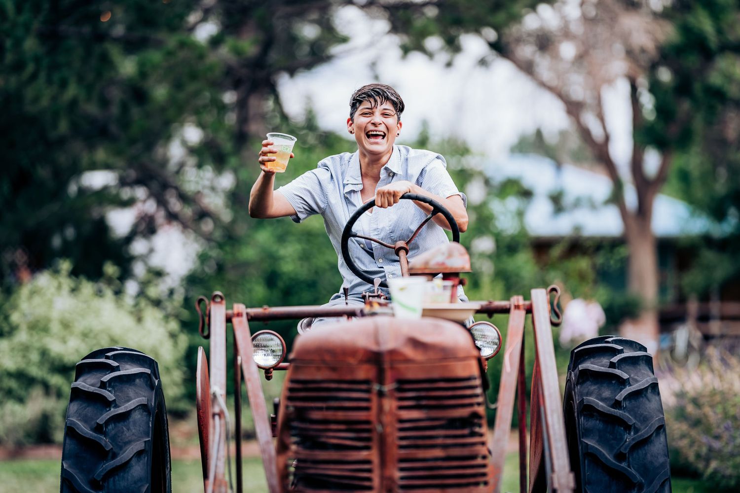 Person wearing a blue shirt celebrates on a vintage red tractor in an outdoor setting.