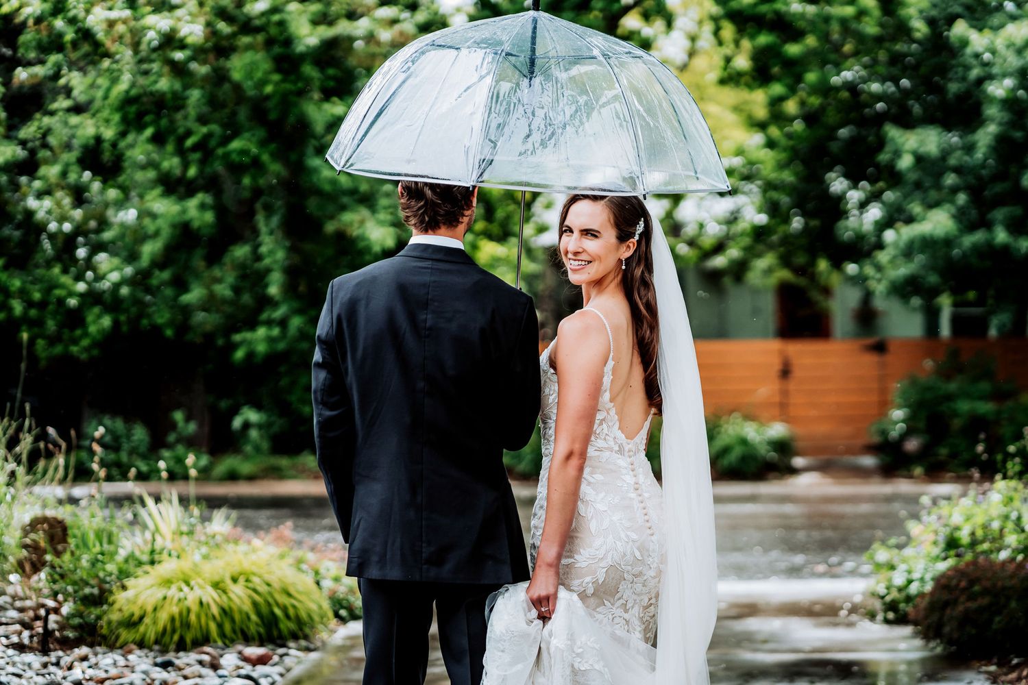 A couple shares a moment under a clear umbrella in a garden setting.