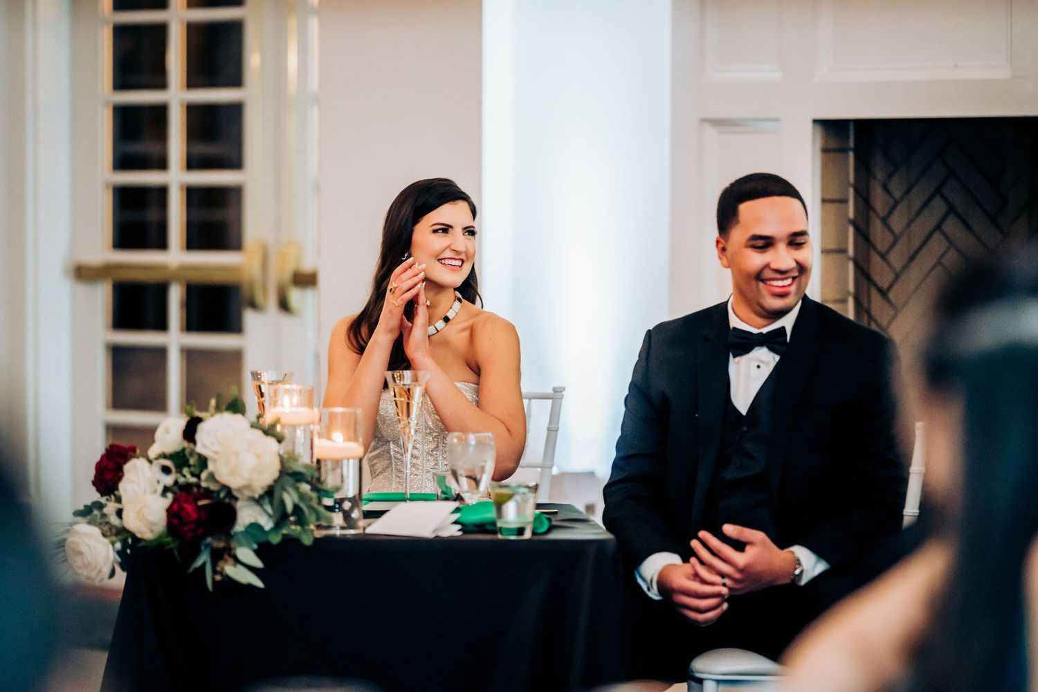Couple shares emotional moment at wedding reception head table with elegant decor.