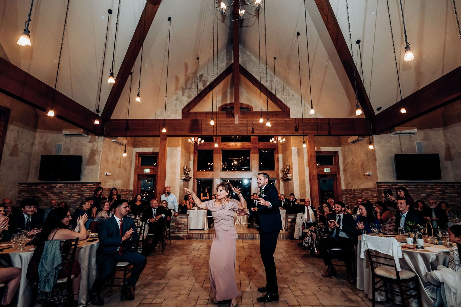 Wedding reception dance in a beautiful vaulted ceiling venue with exposed beams and pendant lighting.