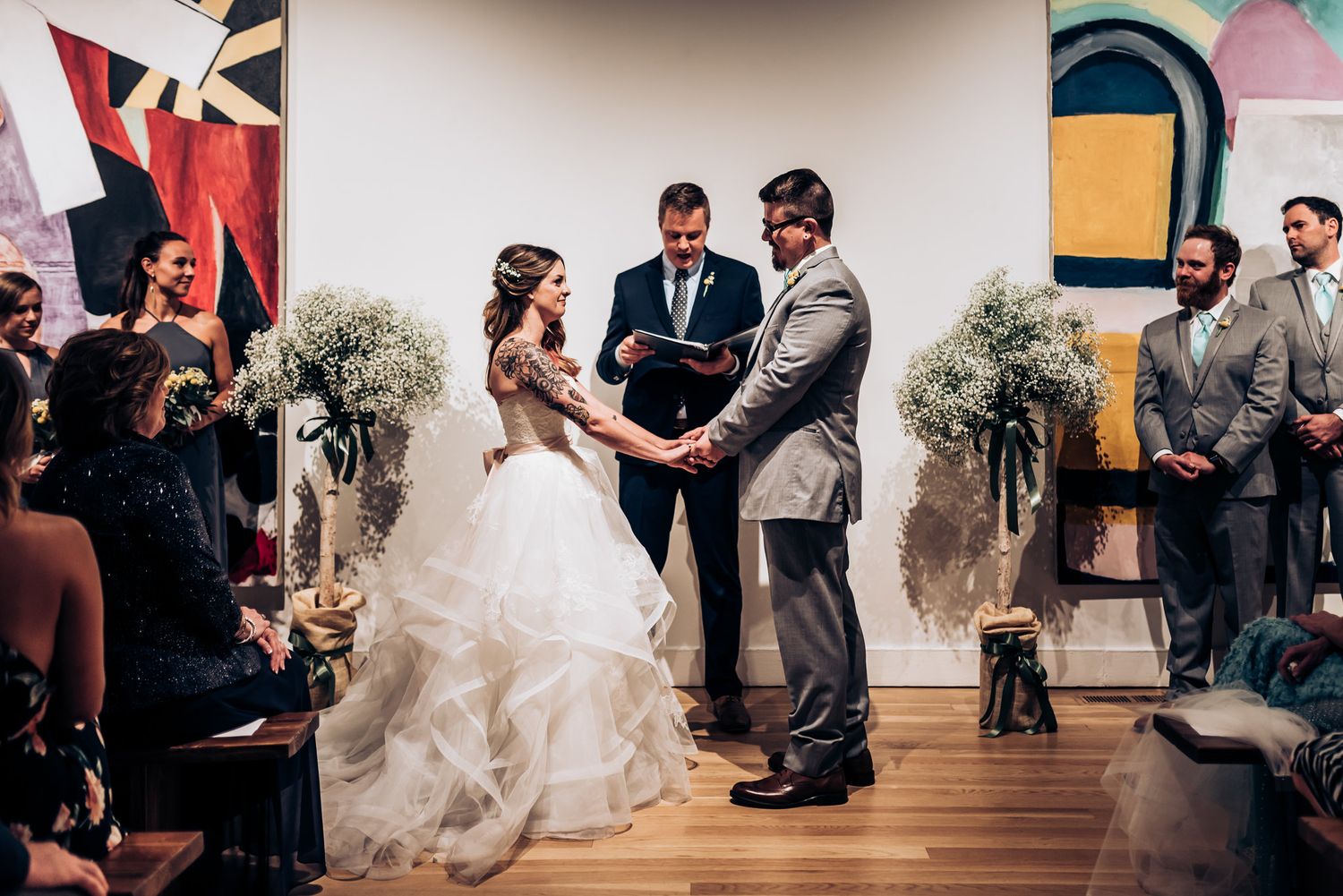 Wedding ceremony in progress inside a modern art gallery with white walls and colorful paintings.