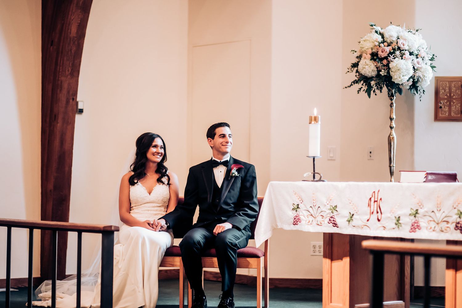 A couple sits on church altar steps during their wedding ceremony.