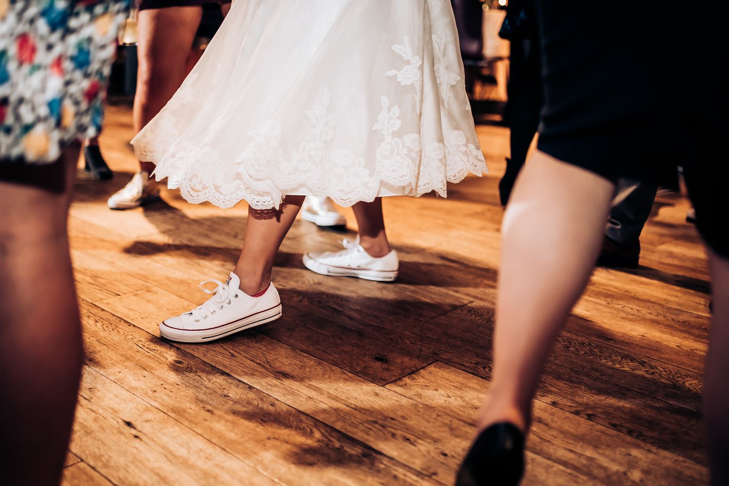 White wedding dress and casual sneakers shown during dance on wooden floor.