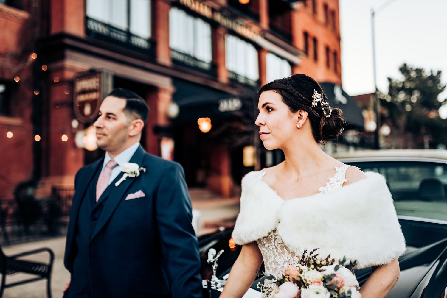 Stylish wedding couple walking in urban setting with brick buildings and city lights.