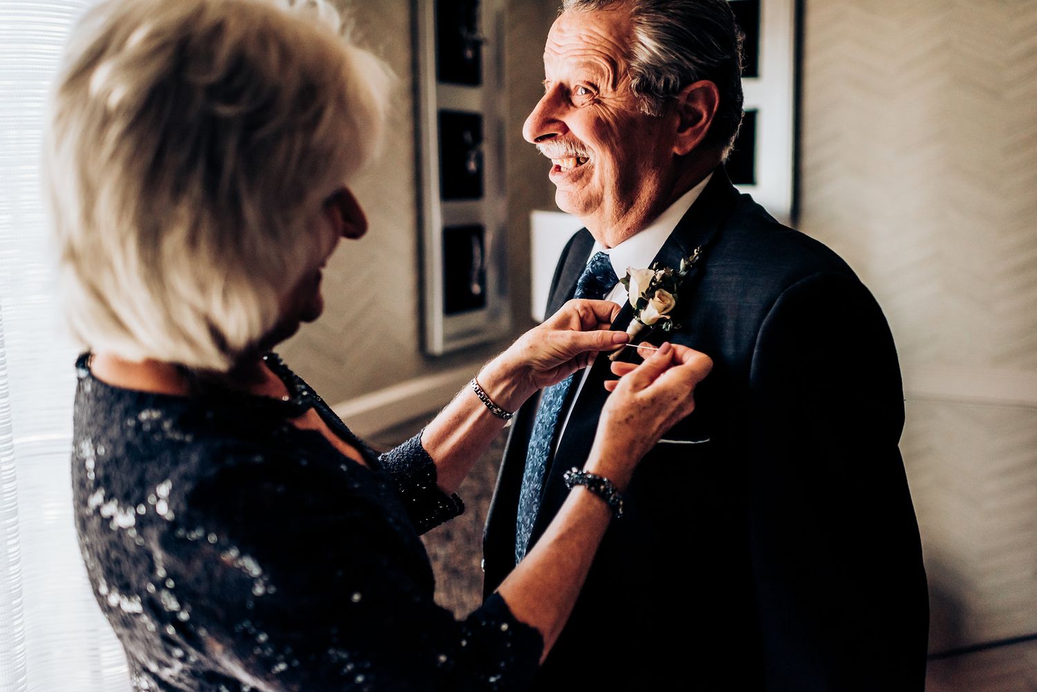 Two people share a joyful moment while adjusting formal attire.