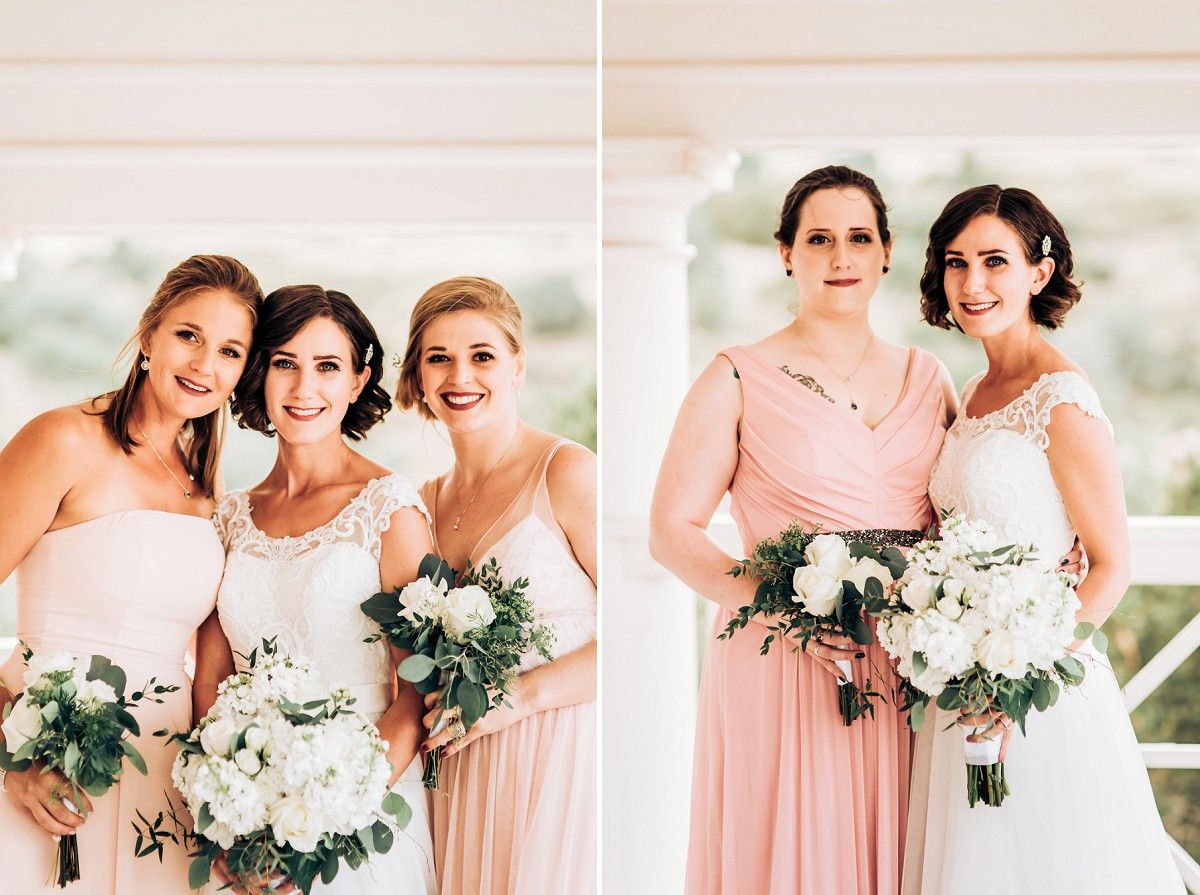 Bridesmaids in blush pink dresses holding white floral bouquets pose together.
